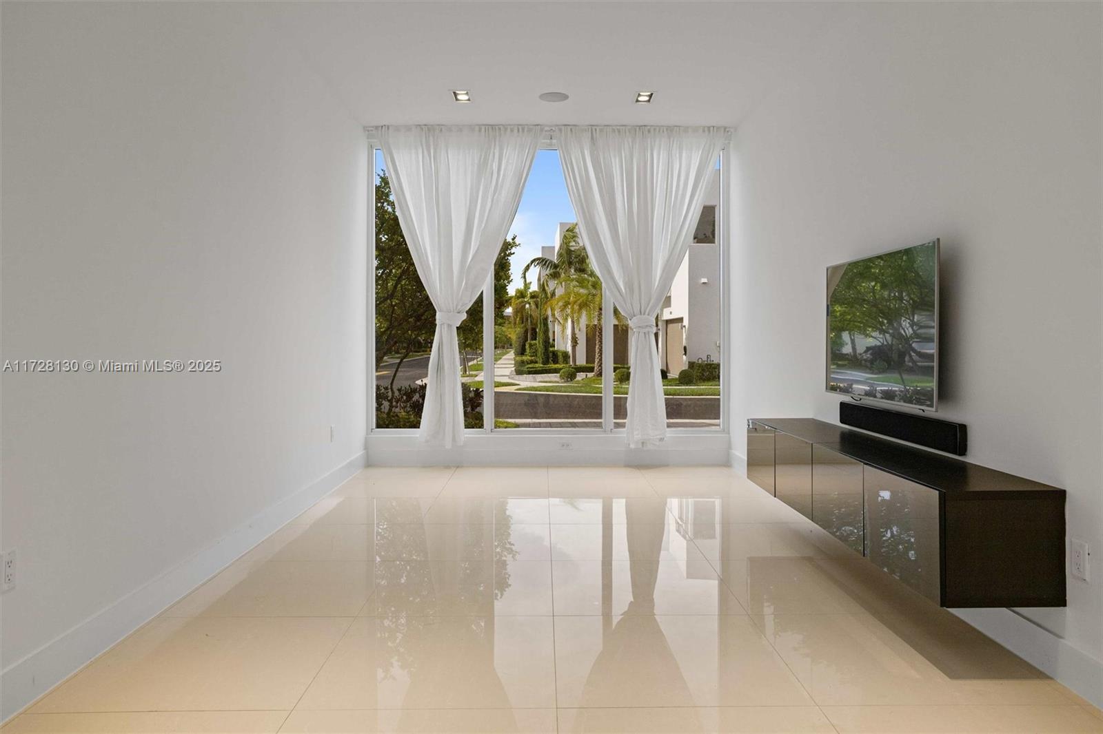 A minimalist living room features white walls, polished tile floors, and a large window view — 10296 NW 74th Ter, Doral FL 33178, DORAL, FL