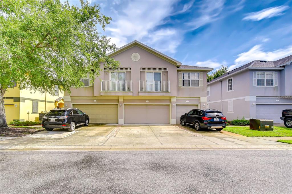 A two-story townhouse exterior with three garage doors and two parked SUVs in the driveway — 27845 PLEASURE RIDE LOOP, WESLEY CHAPEL, FL