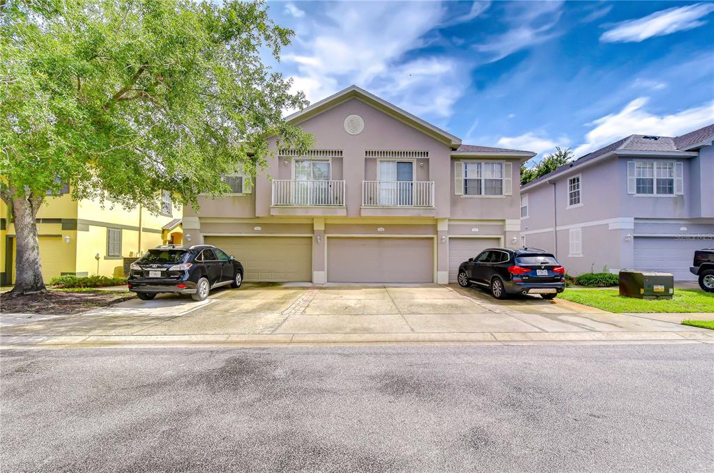 A two-story townhouse exterior with a three-car garage and two parked SUVs — 27845 PLEASURE RIDE LOOP, WESLEY CHAPEL, FL