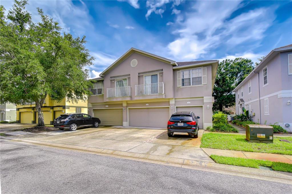 A two-story townhouse exterior features a beige facade, two garage doors, and two upper balconies — 27845 PLEASURE RIDE LOOP, WESLEY CHAPEL, FL
