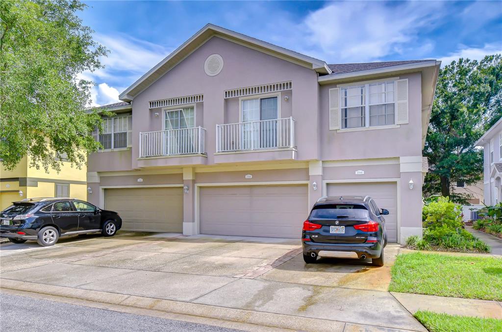 A two-story townhouse exterior with three garage doors, two balconies, and two parked SUVs — 27845 PLEASURE RIDE LOOP, WESLEY CHAPEL, FL