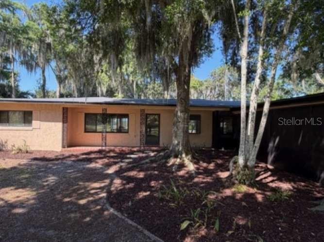 A single-story house with a light-colored exterior sits behind several large, moss-covered oak trees — 930 SHORE DRIVE, KISSIMMEE, FL