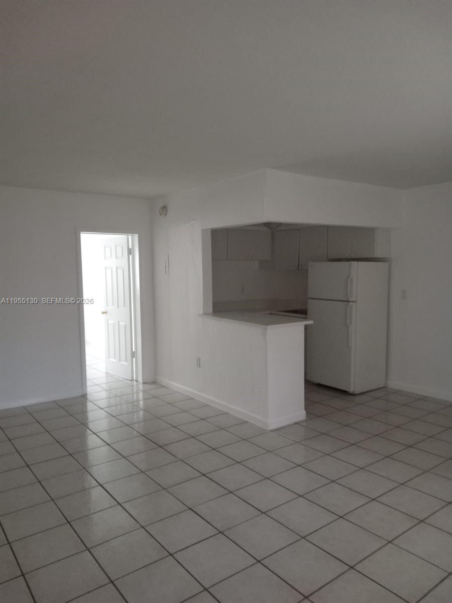 An open-concept living area features white tile flooring and a kitchen with white cabinetry — 1230 W 54th St # 216A, Hialeah FL 33012, HIALEAH, FL