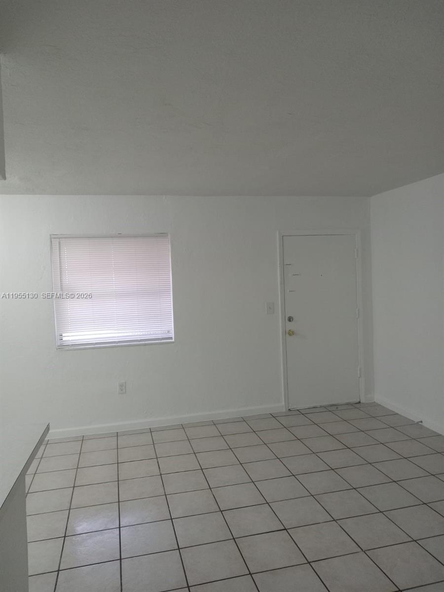 An empty room features white walls, a window with blinds, and light-colored square floor tiles — 1230 W 54th St # 216A, Hialeah FL 33012, HIALEAH, FL