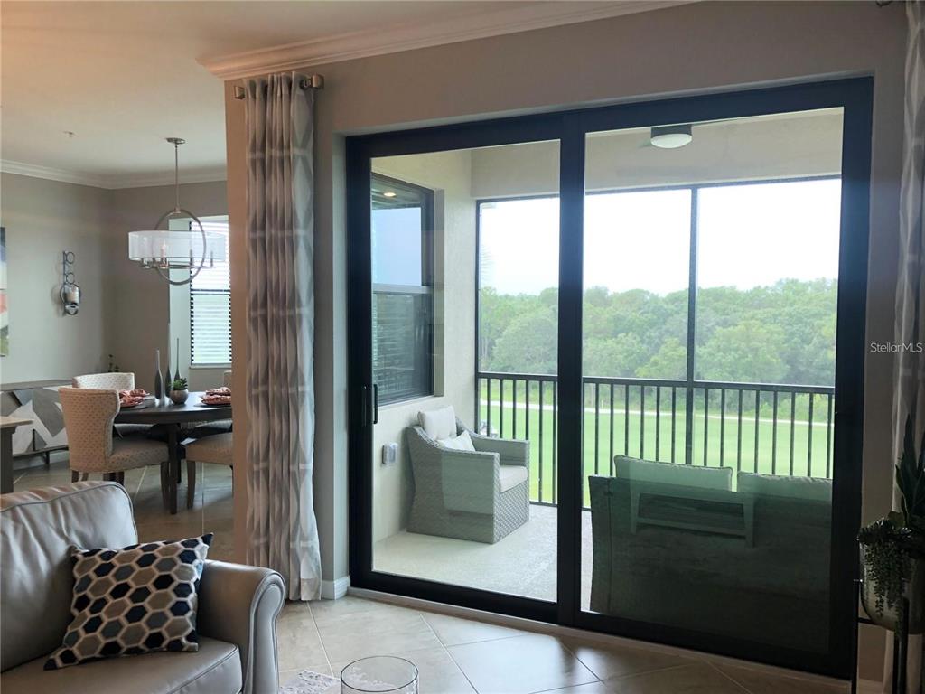 A living room with tile floors looks out through sliding glass doors to a screened balcony — 17510 GAWTHROP DRIVE UNIT 405, LAKEWOOD RANCH, FL
