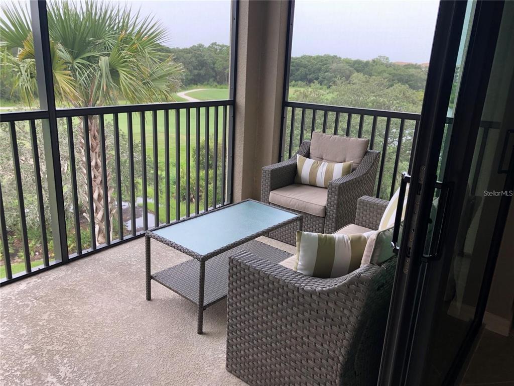 A screened-in balcony features wicker chairs, a glass-top table, and a view of greenery — 17510 GAWTHROP DRIVE UNIT 405, LAKEWOOD RANCH, FL