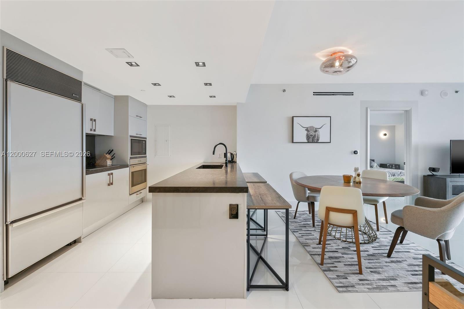 A modern kitchen with a dark island countertop, white cabinetry, and an adjacent dining area — 465 Brickell Ave # 1805, Miami FL 33131, MIAMI, FL