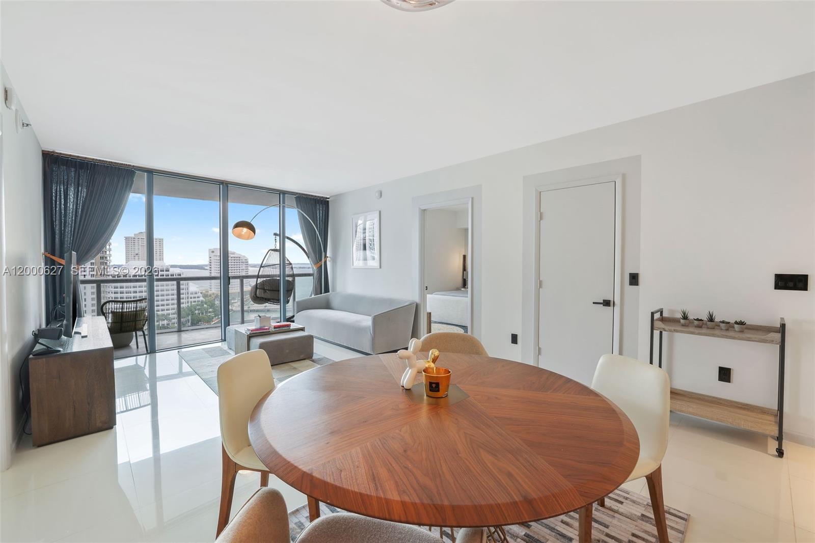 A modern dining and living area features a round wooden table, floor-to-ceiling windows, and balcony — 465 Brickell Ave # 1805, Miami FL 33131, MIAMI, FL