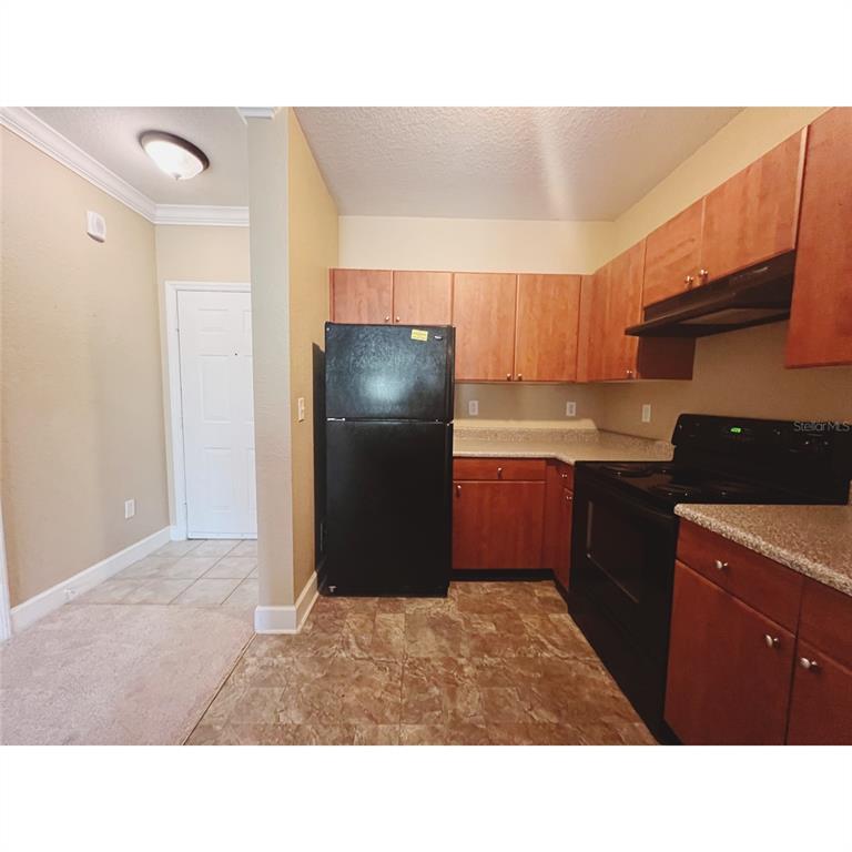 A kitchen features wood cabinets, black appliances, and a tiled floor next to a doorway — 304 E SOUTH STREET UNIT 3019, ORLANDO, FL