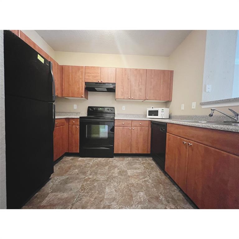 A kitchen features wood cabinets, black appliances, laminate countertops, and patterned vinyl flooring — 304 E SOUTH STREET UNIT 3019, ORLANDO, FL