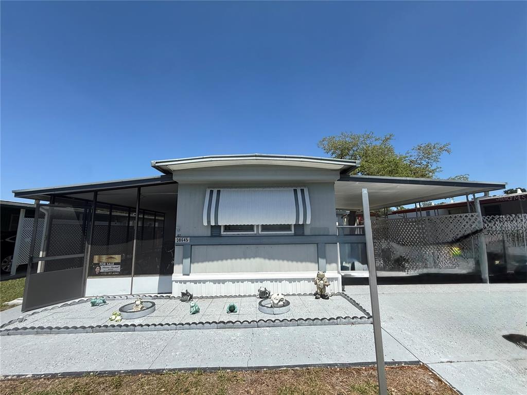 A single-story mobile home features a screened-in porch, a carport, and a small front garden — 38645 REMORA AVENUE, ZEPHYRHILLS, FL