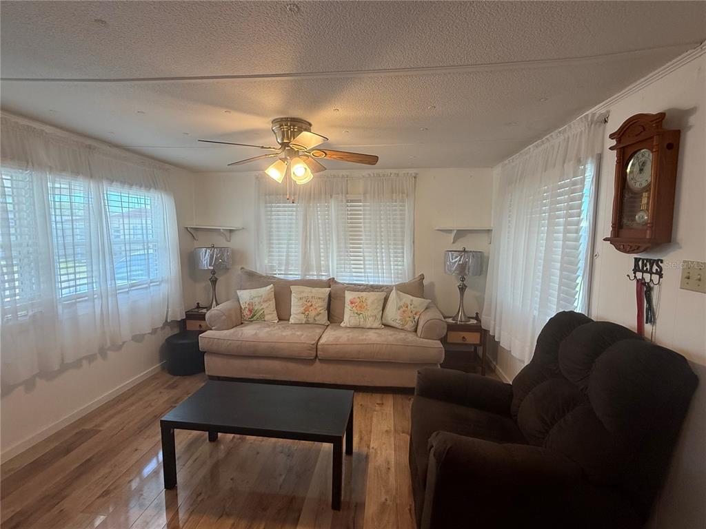 A living room features a beige sofa, a dark recliner, a coffee table, and wood flooring — 38645 REMORA AVENUE, ZEPHYRHILLS, FL