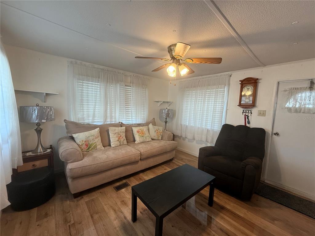 A living room features a beige sofa, a dark recliner, a coffee table, and wood-look flooring — 38645 REMORA AVENUE, ZEPHYRHILLS, FL