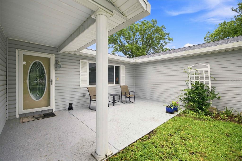 A covered concrete patio features a white column, gray siding, and a glass-paneled front door — 10435 SE 178TH PLACE, SUMMERFIELD, FL