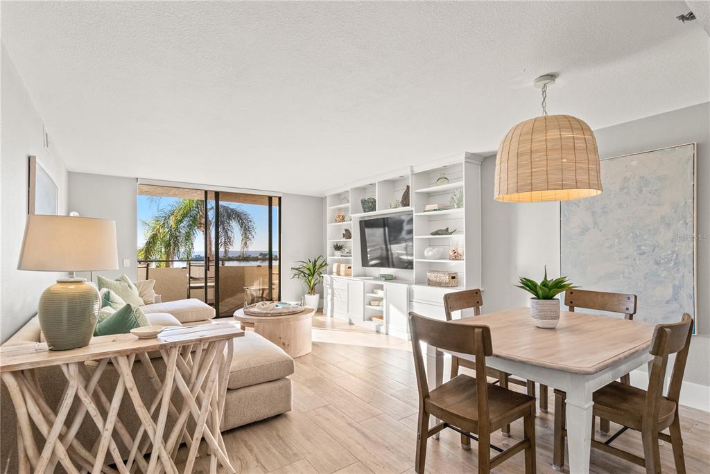 A living and dining area features white built-in shelving, wood-look flooring, and a balcony view — 6035 SEA RANCH DRIVE UNIT 203, HUDSON, FL