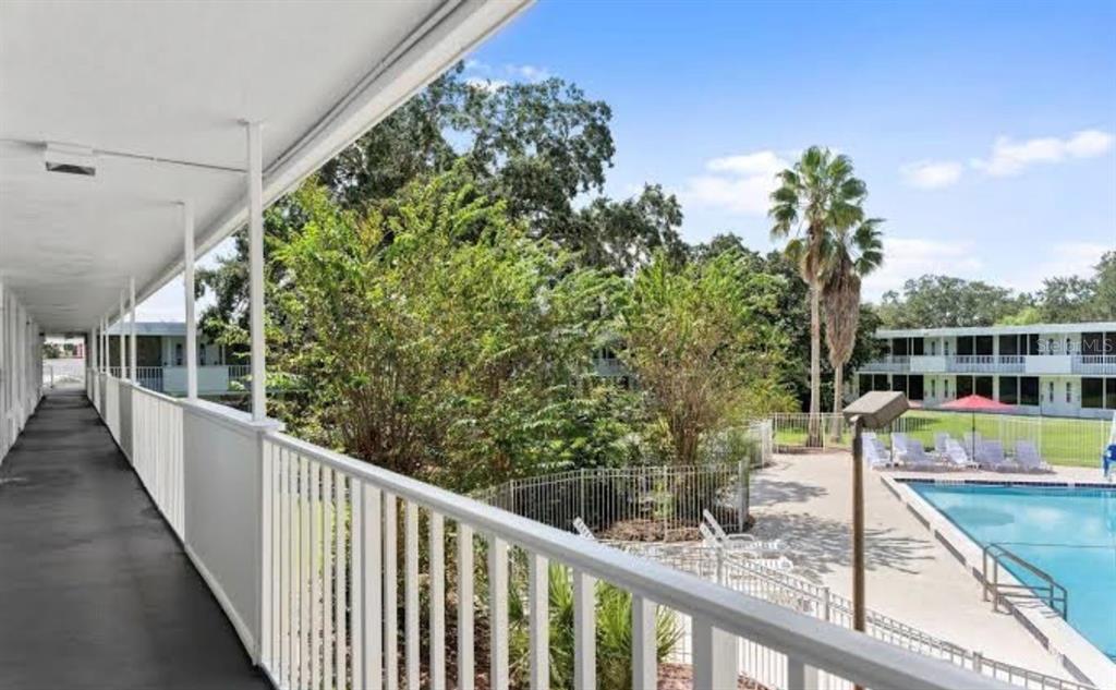An elevated outdoor walkway overlooks a swimming pool and lush trees at an apartment complex — 2930 POLYNESIAN ISLE BOULEVARD UNIT 221, KISSIMMEE, FL