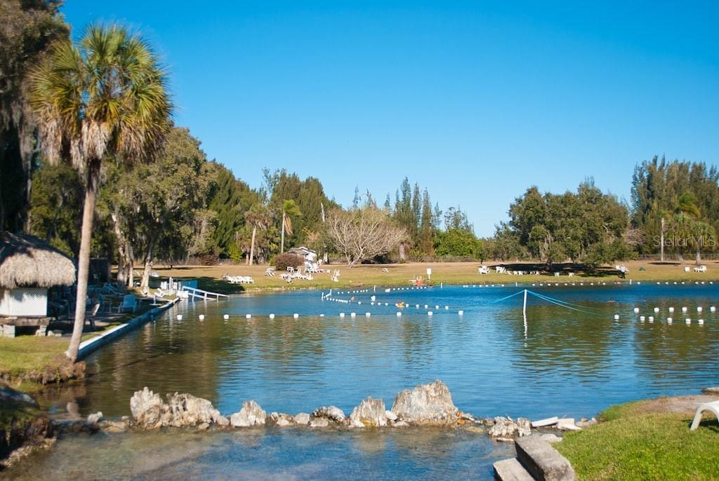 A swimming area with a rope barrier, rocky edge, and surrounding trees under a blue sky — CHANNING AVENUE, NORTH PORT, FL