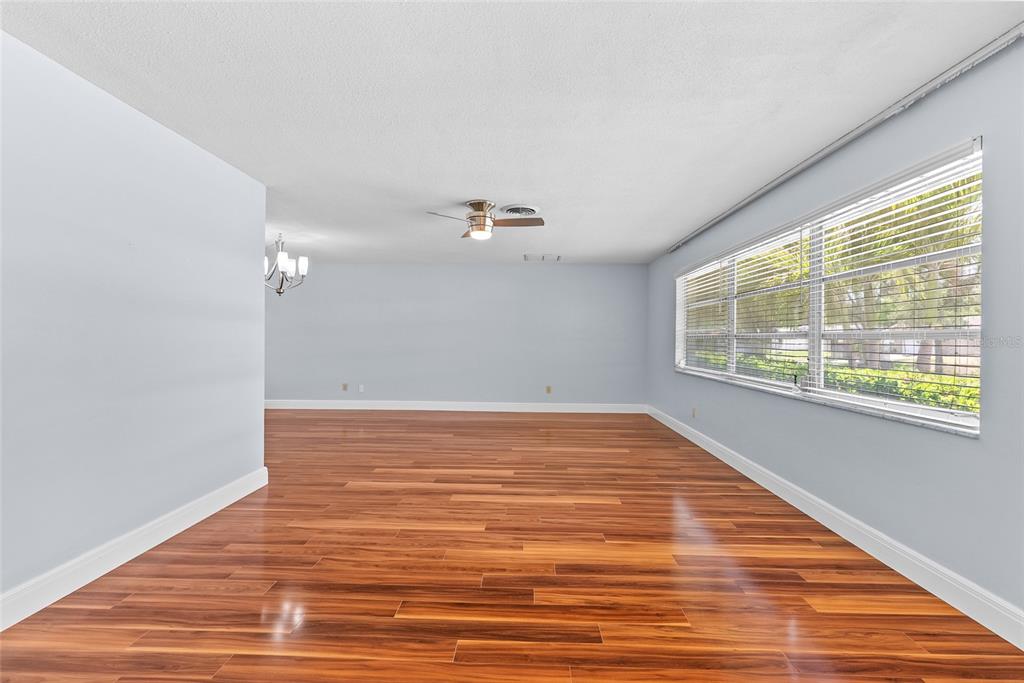An empty room with light blue walls, hardwood flooring, a ceiling fan, and large windows — 1341 RANCHWOOD DRIVE, CLEARWATER, FL