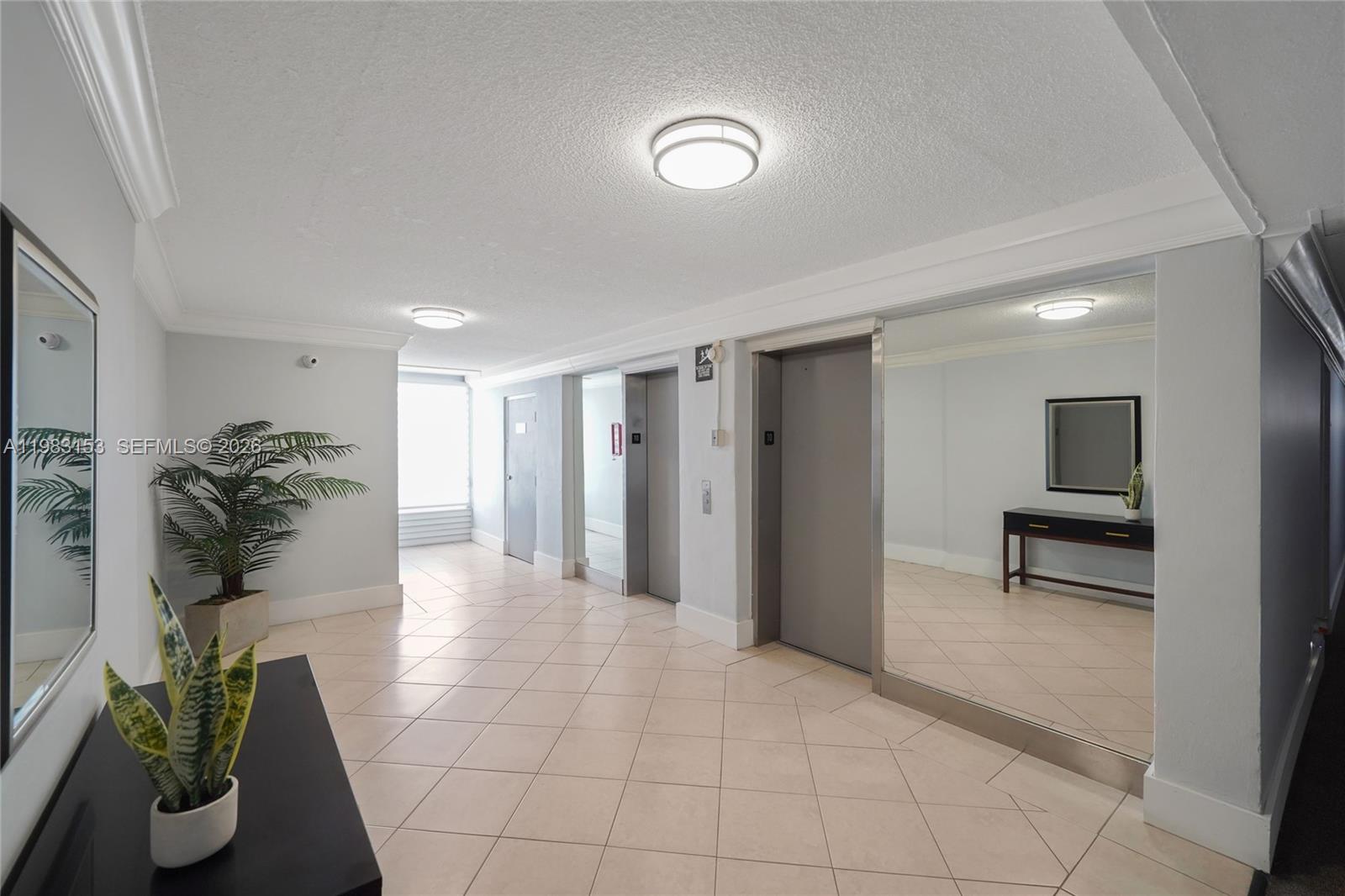 A brightly lit elevator lobby features tiled floors, mirrored walls, and a potted plant — 2000 NE 135th St # 1010, North Miami FL 33181, NORTH MIAMI, FL