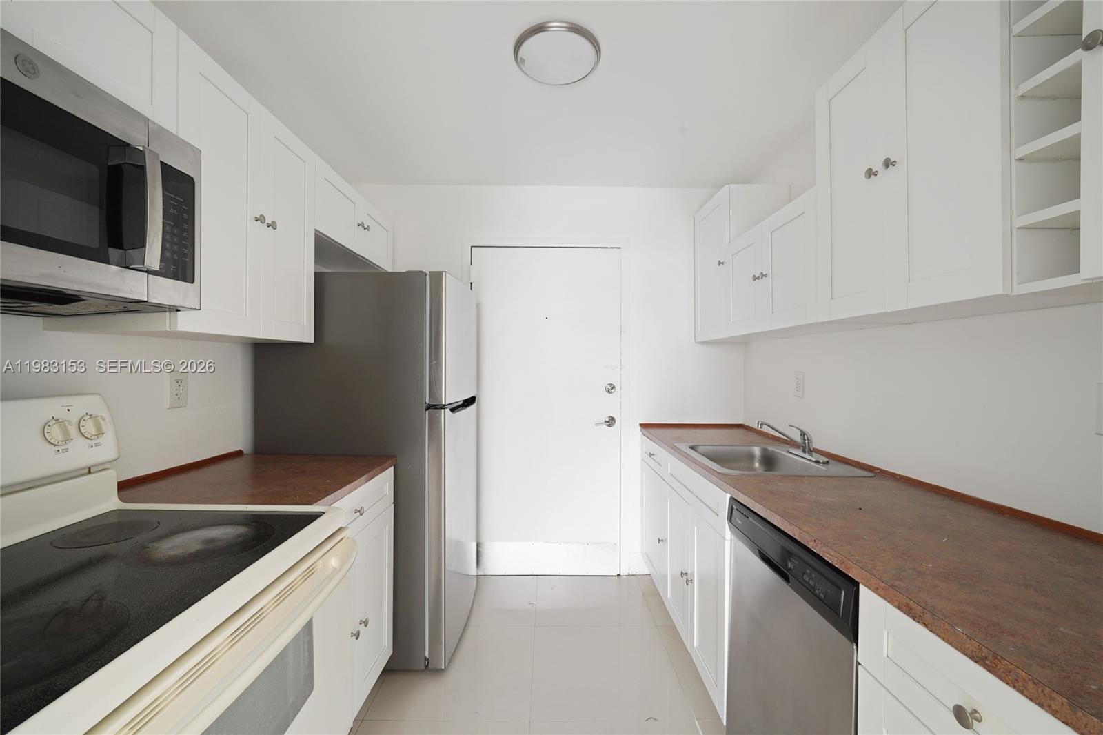 A galley kitchen features white cabinets, stainless steel appliances, and reddish-brown laminate countertops — 2000 NE 135th St # 1010, North Miami FL 33181, NORTH MIAMI, FL