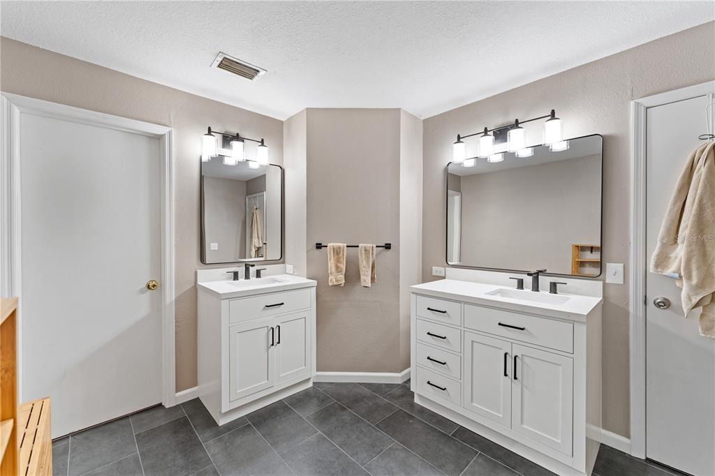 A bathroom features two white vanities with black hardware, rectangular mirrors, and dark tile flooring — 9758 FOX HOLLOW ROAD, TAMPA, FL