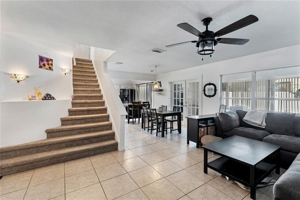 An open-concept living and dining area features a carpeted staircase, tile flooring, and a ceiling fan — 9758 FOX HOLLOW ROAD, TAMPA, FL