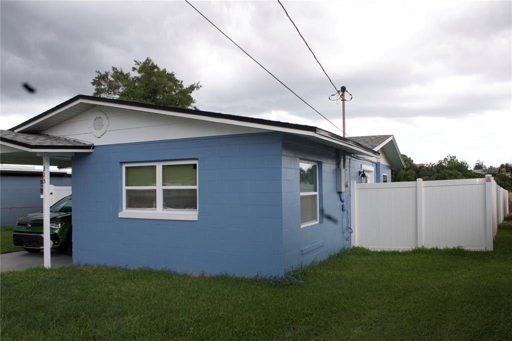 A blue concrete block house with a white fence and a carport on a lawn — 315 AMADOR CIRCLE, ORLANDO, FL