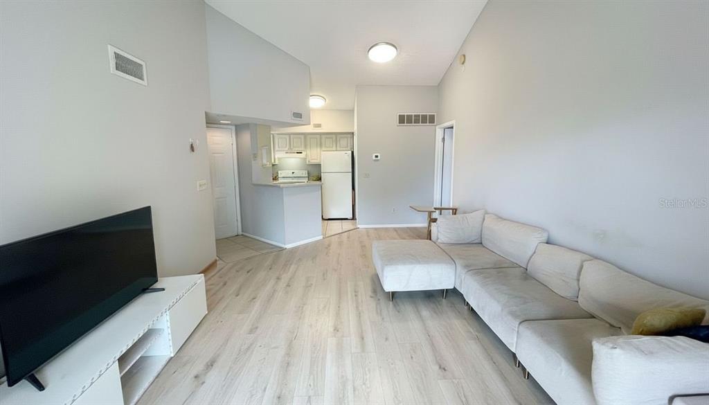A living room with light wood-look flooring, a white sectional sofa, and an adjacent kitchen — 1972 LAKE ATRIUMS CIRCLE UNIT 200, ORLANDO, FL