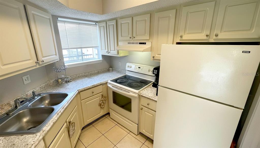 A kitchen features white cabinets, a white stove, a double sink, and speckled countertops — 1972 LAKE ATRIUMS CIRCLE UNIT 200, ORLANDO, FL