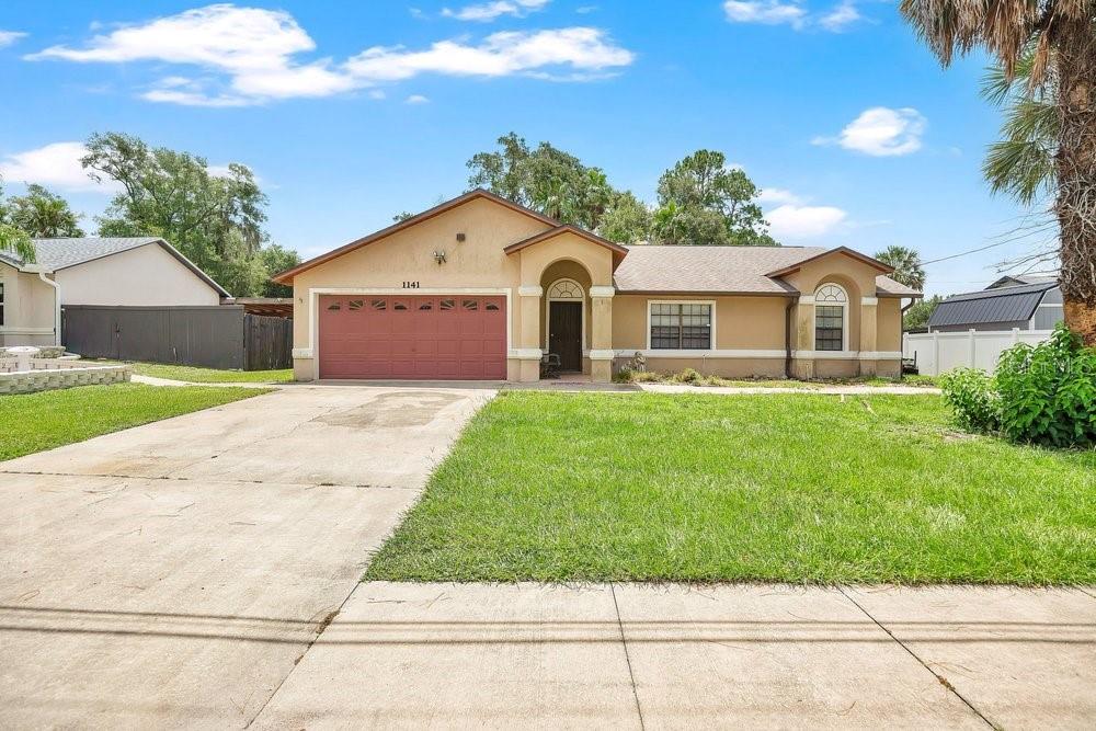 A single-story tan house with a red garage door and a concrete driveway — 1141 DOYLE ROAD, DELTONA, FL