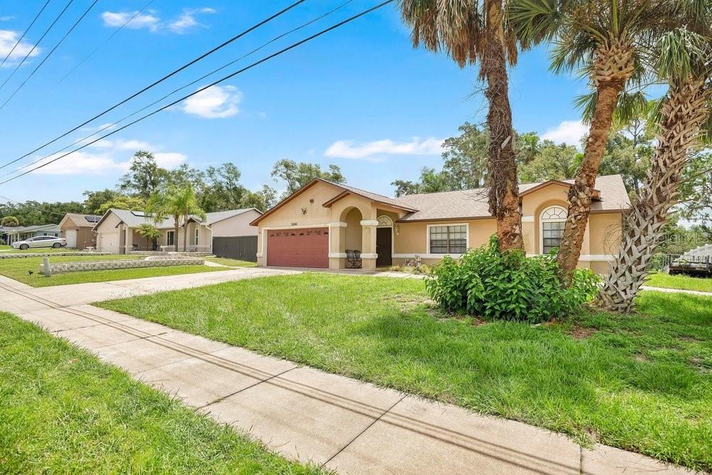 A single-story suburban house with a tan stucco exterior, a red garage door, and palm trees — 1141 DOYLE ROAD, DELTONA, FL