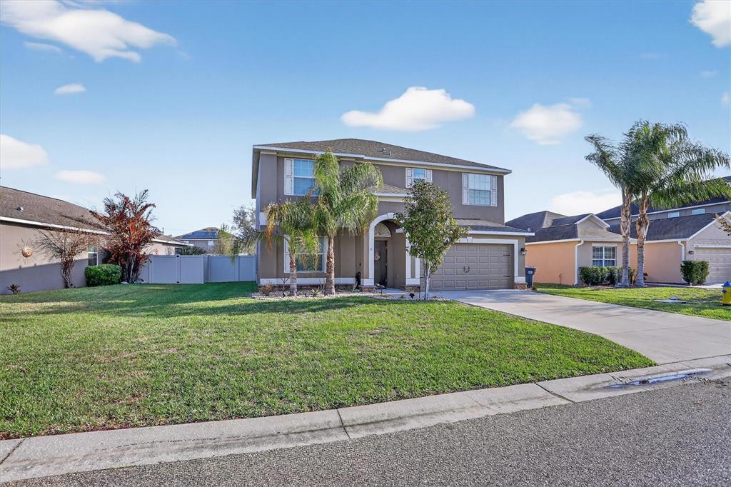 A two-story suburban house with a tan exterior, a two-car garage, and a front lawn — 13908 TENSAW DRIVE, HUDSON, FL
