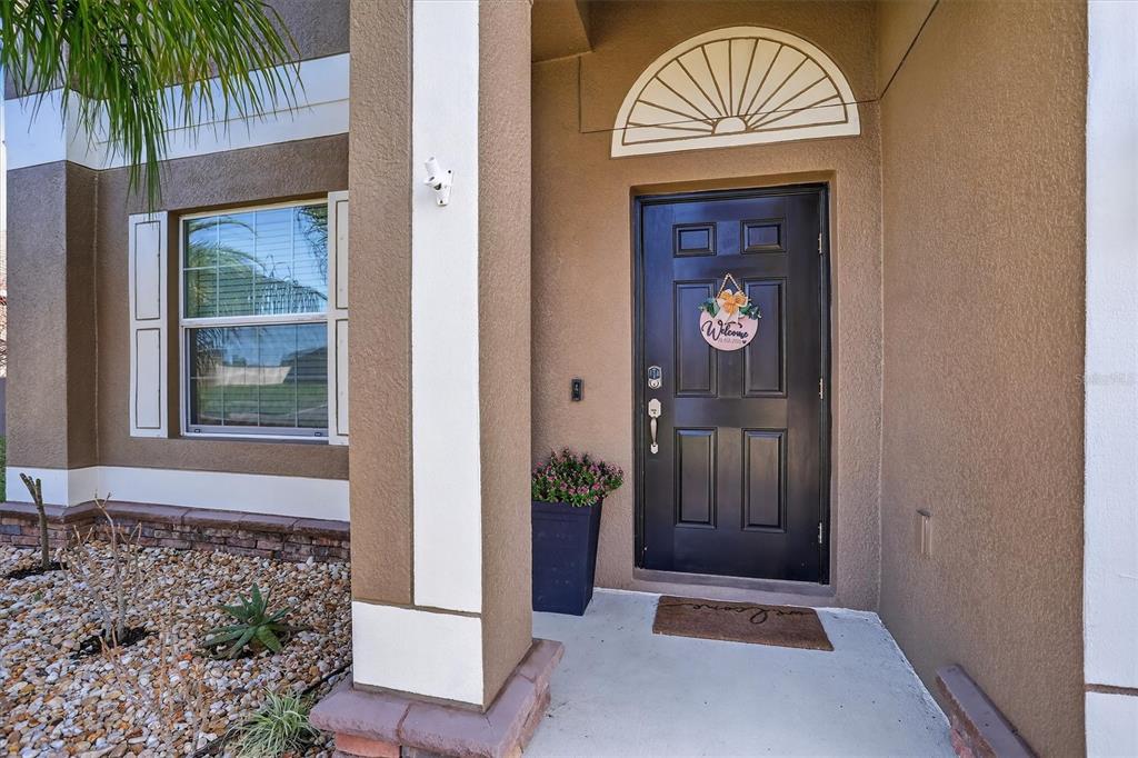 A front entryway with a black door, a welcome sign, and a stone-covered garden bed — 13908 TENSAW DRIVE, HUDSON, FL