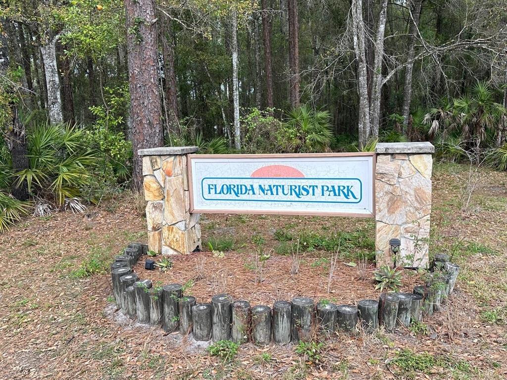 A stone sign for Florida Naturist Park stands in a wooded area with log edging — GRANDVILLE, HUDSON, FL