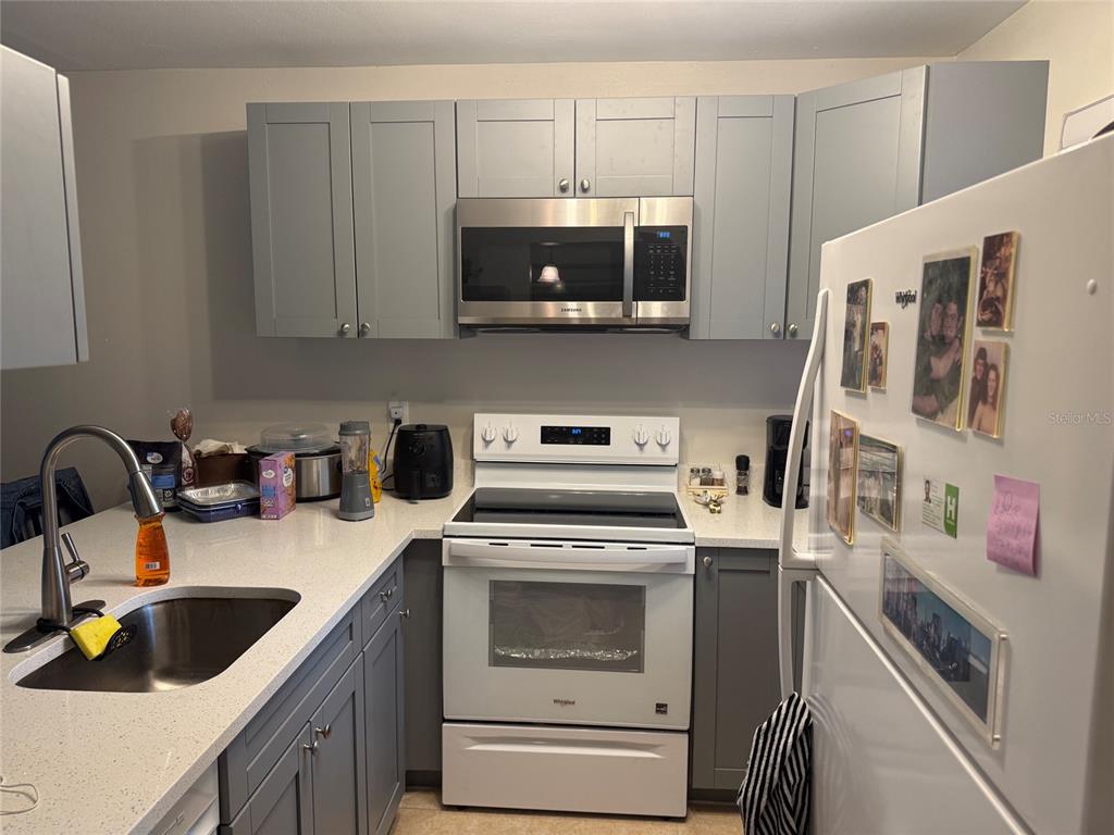 A kitchen features gray cabinets, white countertops, a white oven, and a stainless steel microwave — 39132 COUNTY RD. 54 UNIT 2056, ZEPHYRHILLS, FL