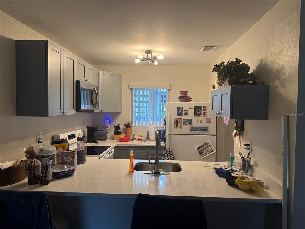 A kitchen features gray cabinets, white countertops, a breakfast bar, and stainless steel appliances — 39132 COUNTY RD. 54 UNIT 2056, ZEPHYRHILLS, FL