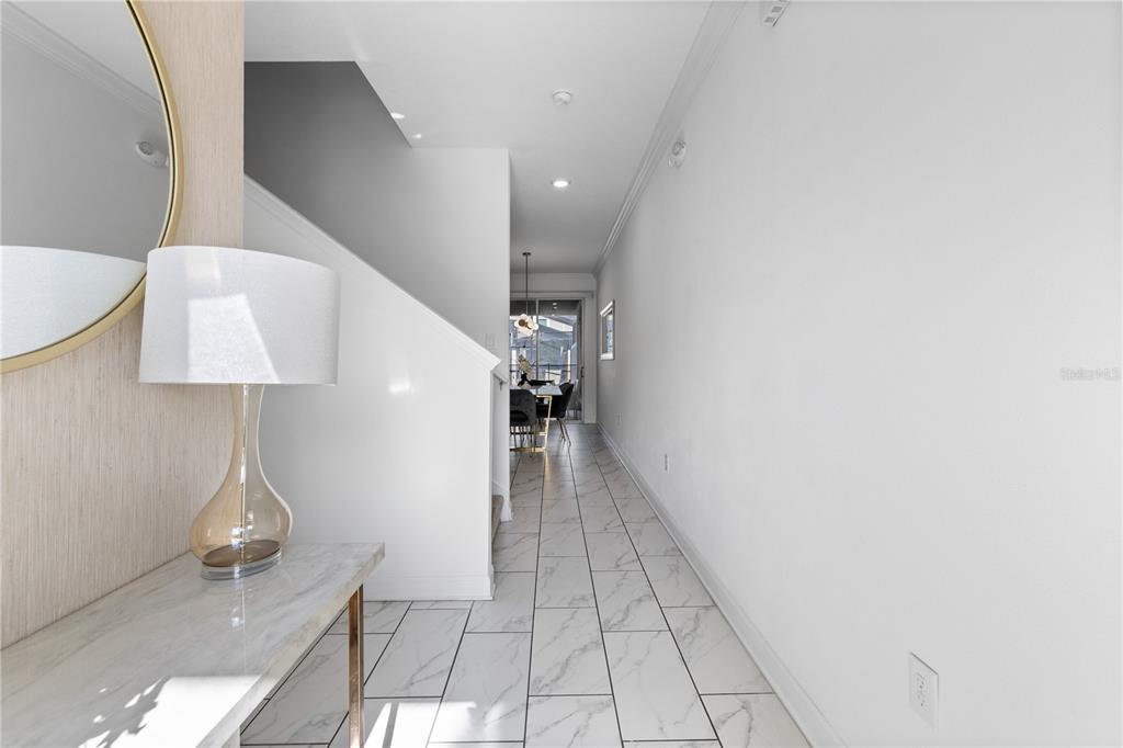 A hallway with white marble-look tile flooring leads toward a dining area and sliding doors — 2970 PROTAGONIST STREET, KISSIMMEE, FL