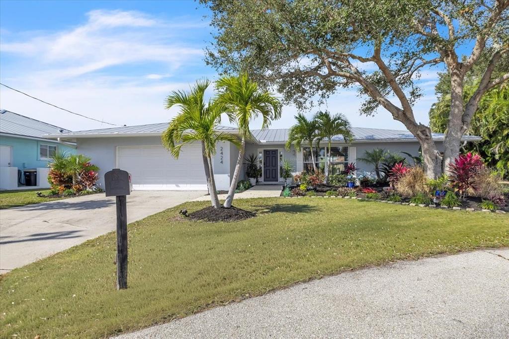 A single-story house with a metal roof, white garage door, and tropical landscaping — 2424 ROSA LANE, PUNTA GORDA, FL