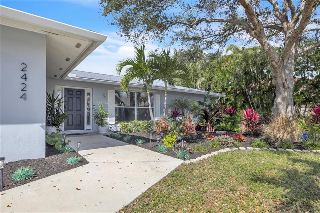 A light gray house features a dark front door, a concrete walkway, and tropical landscaping — 2424 ROSA LANE, PUNTA GORDA, FL