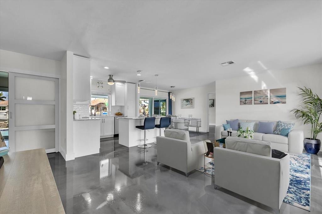 An open-concept living room and kitchen featuring glossy gray floors and white cabinetry — 2424 ROSA LANE, PUNTA GORDA, FL