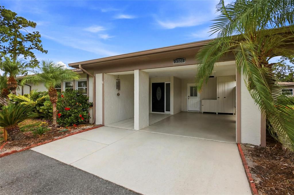 A single-story house exterior features a concrete driveway, a covered carport, and tropical landscaping — 3721 COLLINS STREET UNIT 812, SARASOTA, FL