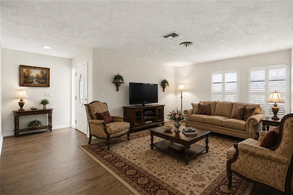 A living room features a tan sofa, two armchairs, a television console, and wood flooring — 3721 COLLINS STREET UNIT 812, SARASOTA, FL
