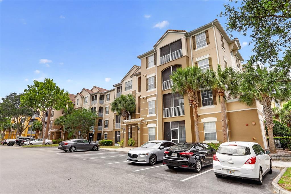 A multi-story apartment building with tan stucco siding and screened balconies sits above a parking lot — 3332 ROBERT TRENT JONES DRIVE UNIT 40203, ORLANDO, FL