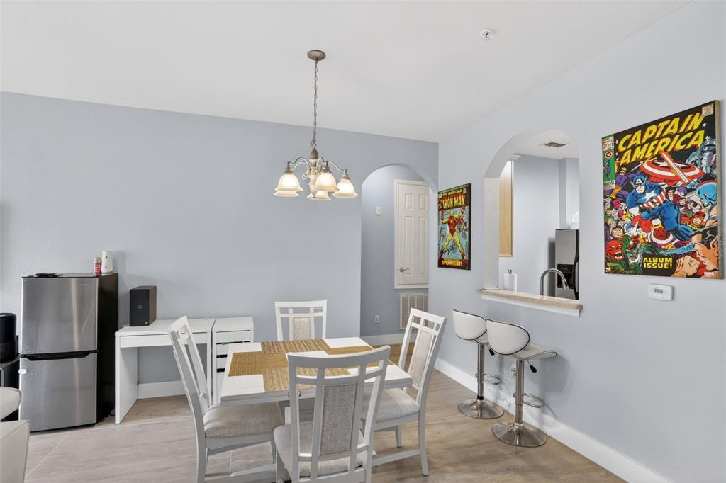 A dining area features a white table, four chairs, a breakfast bar, and superhero wall art — 3332 ROBERT TRENT JONES DRIVE UNIT 40203, ORLANDO, FL