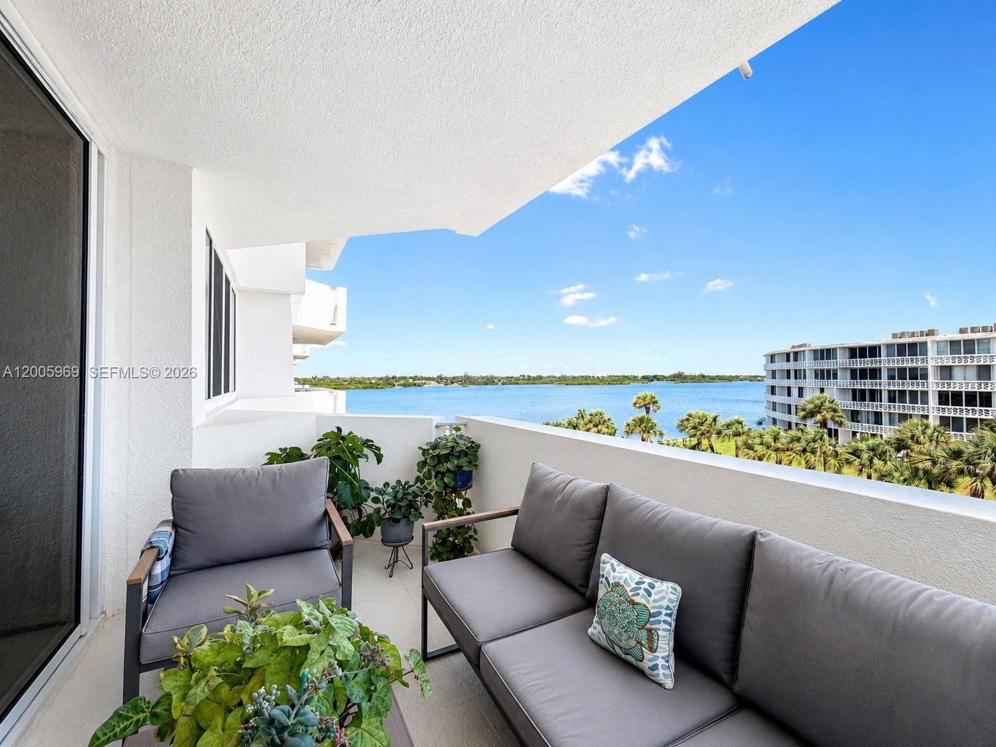 A balcony with gray patio furniture overlooks a body of water and palm trees — 2773 S Ocean Blvd # 4070, Palm Beach FL 33480, PALM BEACH, FL