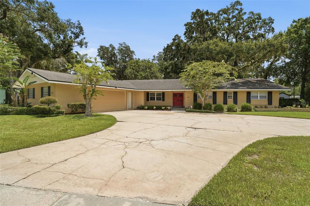 A single-story ranch-style house with a tan exterior, red front door, and a cracked concrete driveway — 421 ELLIOTT AVENUE, SANFORD, FL