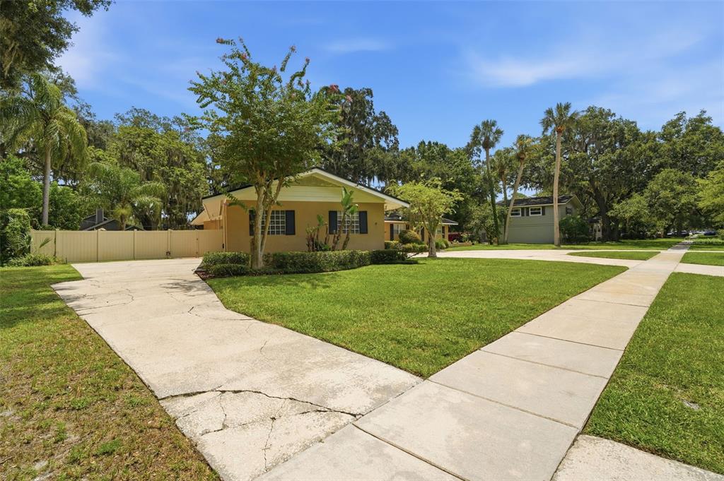 A tan single-story house with a cracked concrete driveway and a large green front lawn — 421 ELLIOTT AVENUE, SANFORD, FL