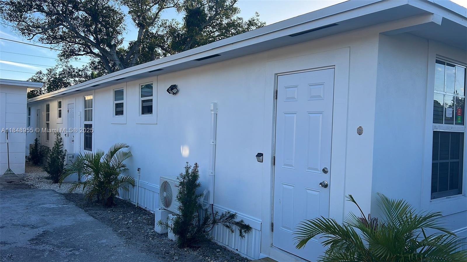 A white exterior wall features a door, several windows, and an outdoor air conditioning unit — 9674 NW 10th Ave, Miami FL 33150, MIAMI, FL