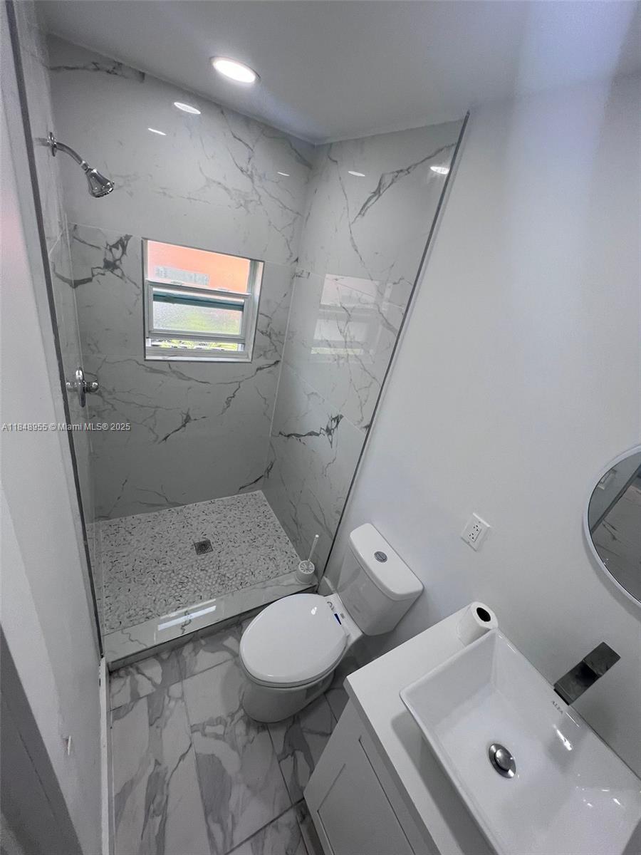 A modern bathroom features a walk-in shower with marble-patterned tiles, a toilet, and a vanity — 9674 NW 10th Ave, Miami FL 33150, MIAMI, FL