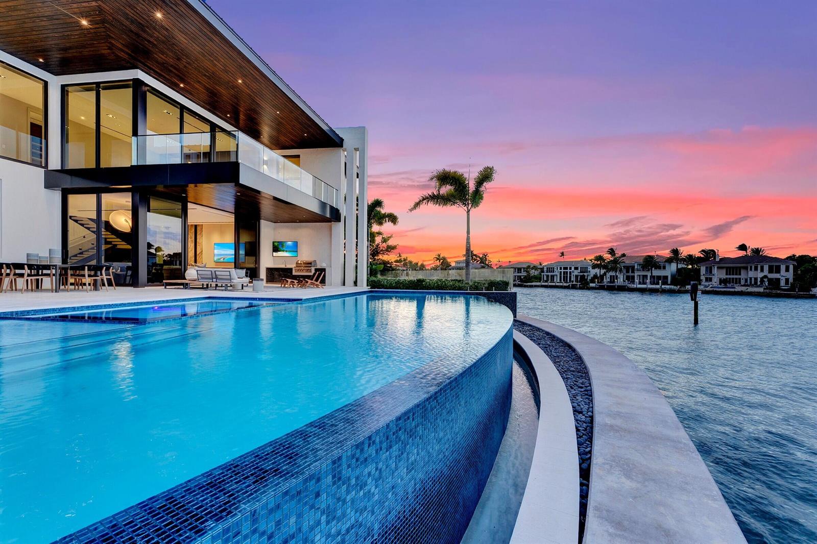 An infinity pool overlooks a waterfront view at sunset next to a modern two-story home — 829 Orchid Drive, Boca Raton FL 33432, BOCA RATON, FL